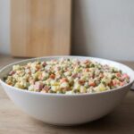 Салат оливье классический с колбасой в белой миске на кухонном столе